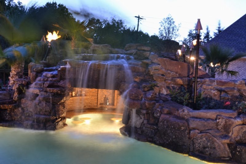 Bassin éclairé de nuit, large cascade sur rocher et torches allumées
